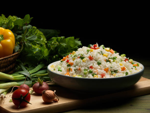 A bowl of colorful vegetable rice served on a wooden board with fresh herbs and vegetables in the background.