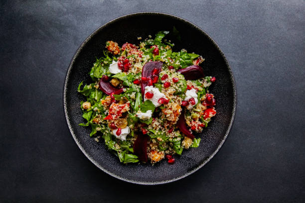 A colorful quinoa salad topped with yogurt, beets, pomegranate seeds, and greens in a black bowl