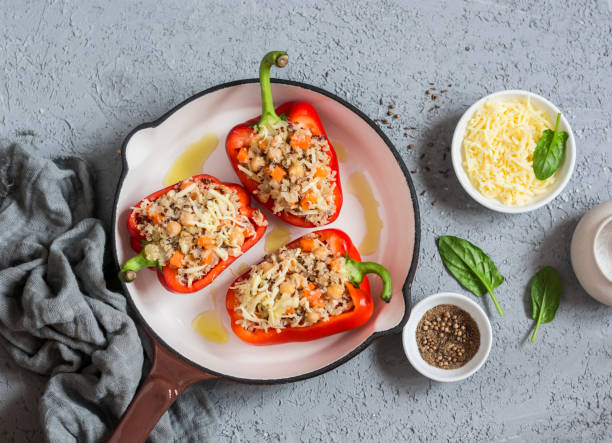 Stuffed red bell peppers in a skillet with cheese and herbs, surrounded by seasonings and fresh spinach.