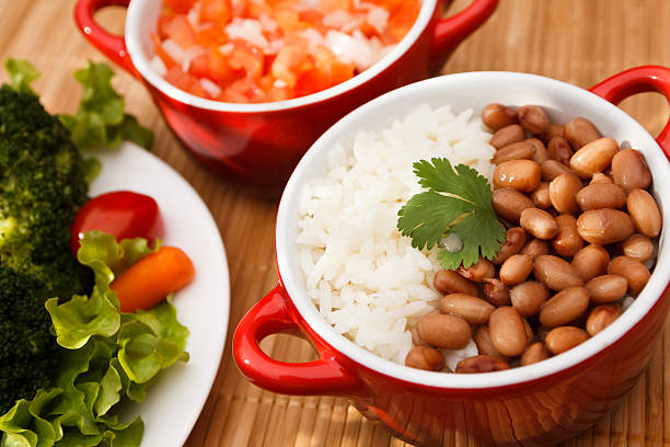 A plate of rice served with black beans, accompanied by two bowls of black beans and white rice on a wooden table.