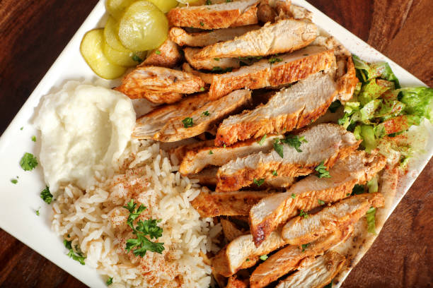 A plate of sliced grilled chicken served with rice, mashed potatoes, pickles, and a side of lettuce.