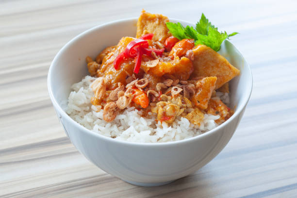 Bowl of rice topped with fried tofu, peanuts, and garnished with red chili and herbs