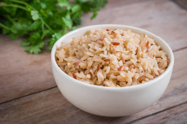 A bowl of cooked brown rice with a sprinkle of herbs in the background