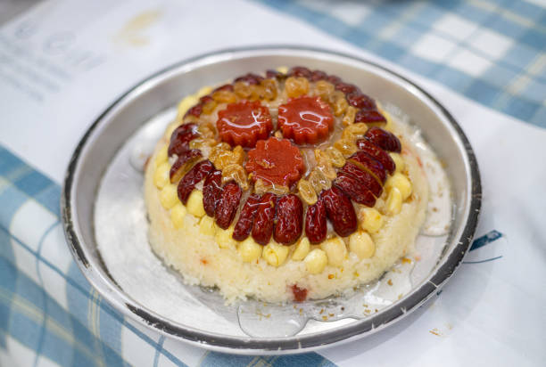 A beautifully decorated cake topped with red dates, nuts, and gelatin, served on a round metallic plate.