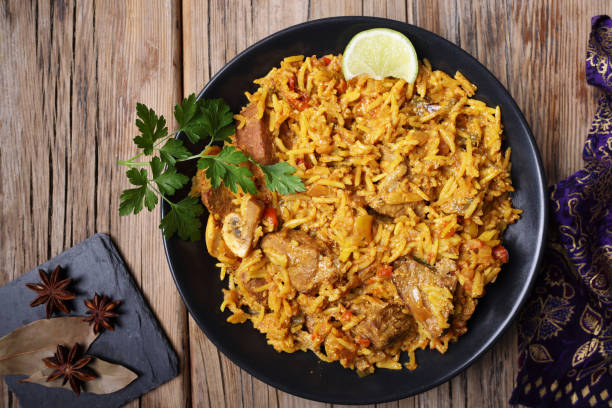 A delicious plate of rice dish with meat, garnished with lime and herbs, on a wooden table.