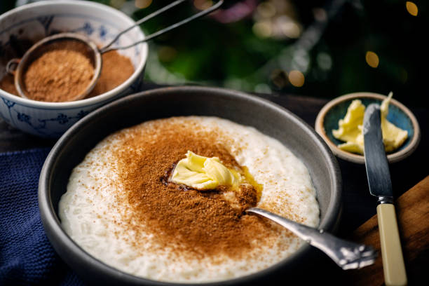 A bowl of creamy porridge topped with butter and a dusting of cinnamon, next to small dishes of cinnamon powder and a butter knife.