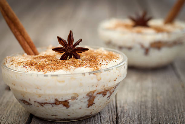 Bowls of creamy rice pudding topped with cinnamon and star anise on a rustic wooden surface.