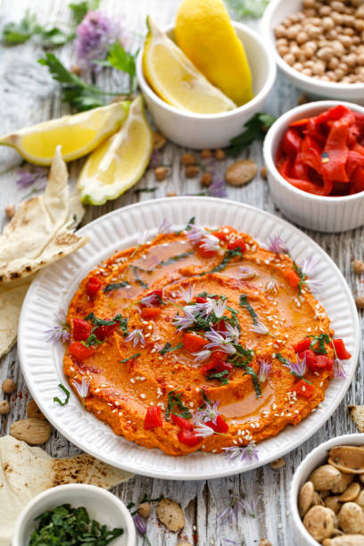 A colorful plate of red pepper dip garnished with herbs, served with lemon slices and other ingredients.