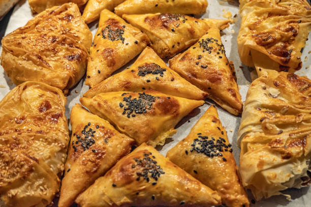 A variety of golden-brown baked pastries arranged on a baking sheet, some topped with black and white sesame seeds.