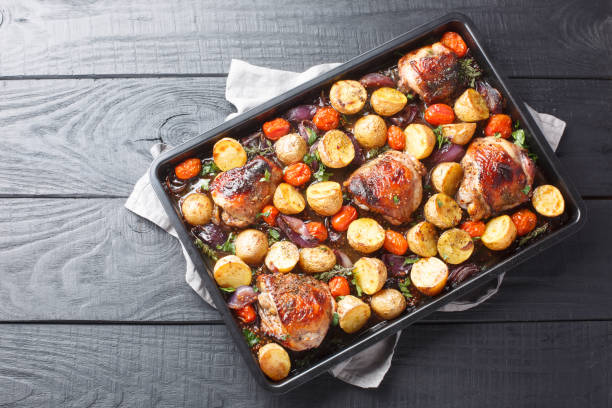 A tray of roasted chicken thighs with baby potatoes and cherry tomatoes on a wooden table.