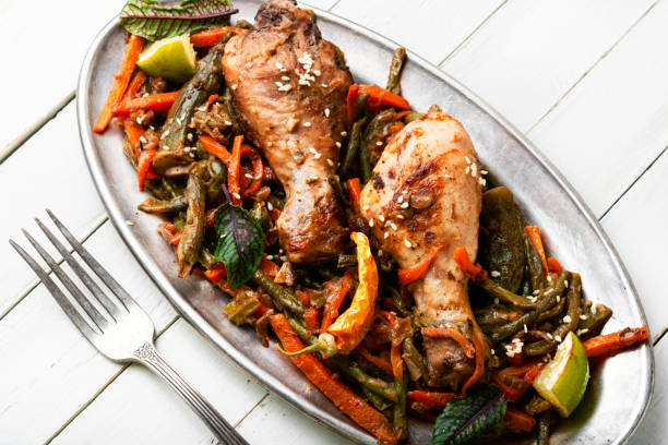 A platter of roasted chicken drumsticks served with colorful mixed vegetables including carrots, green beans, and red peppers, garnished with herbs and lime wedges.