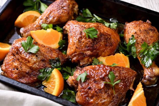 Roasted chicken pieces garnished with parsley and orange slices on a baking tray.