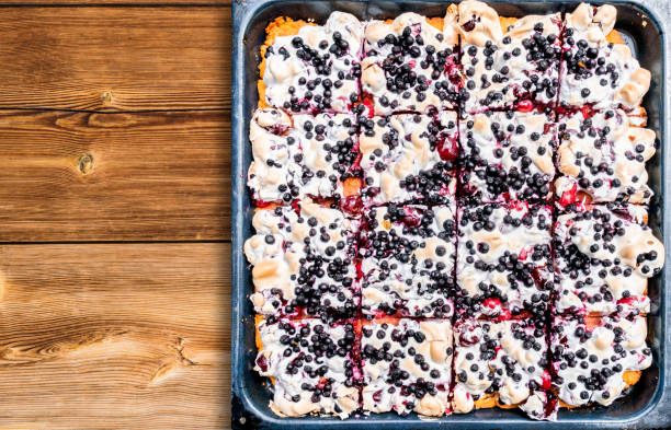 A square baking tray filled with a dessert topped with whipped cream and blueberries, resting on a wooden surface.