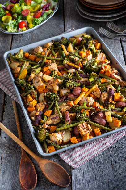 A tray of roasted vegetables and chicken, including broccoli, sweet potatoes, and green beans, with a salad in the background.