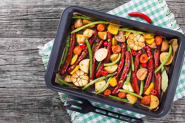 A colorful assortment of roasted vegetables and sausages in a baking tray.