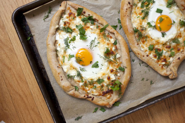 Two delicious pieces of khachapuri with melted cheese, herbs, and a sunny-side-up egg, served on a baking tray.