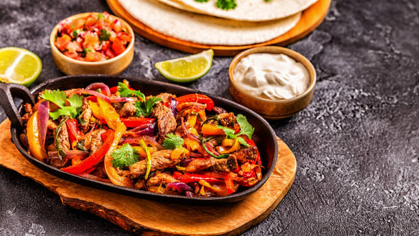 A sizzling plate of fajitas with colorful bell peppers, onions, and fresh herbs served with tortillas, salsa, and sour cream.