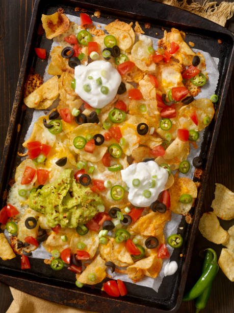 A tray of nachos topped with guacamole, sour cream, jalapeños, diced tomatoes, and black olives.