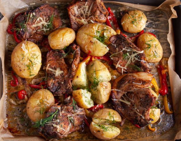 A platter of roasted pork chops and potatoes garnished with herbs on a parchment-lined baking tray.