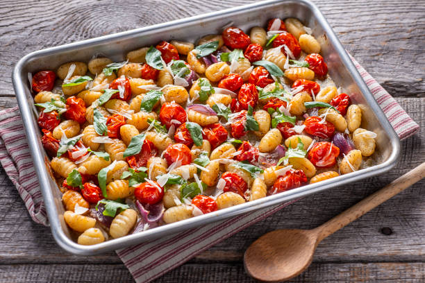 A baking dish filled with gnocchi, cherry tomatoes, and fresh basil on a rustic wooden table.