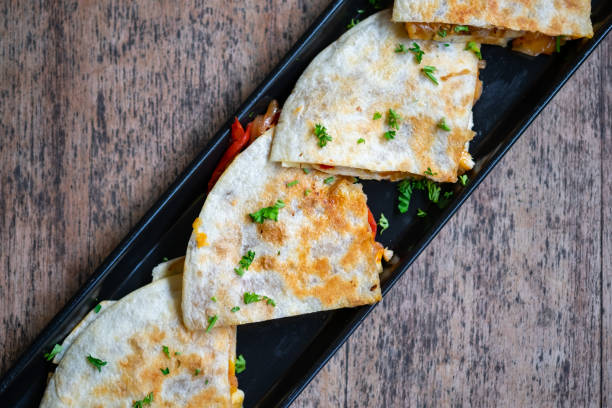 A plate of golden-brown quesadillas garnished with fresh herbs, placed on a dark wooden table.