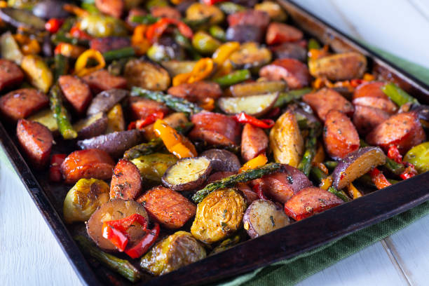 A tray of roasted vegetables and sausage, featuring colorful bell peppers, asparagus, and a variety of potatoes.