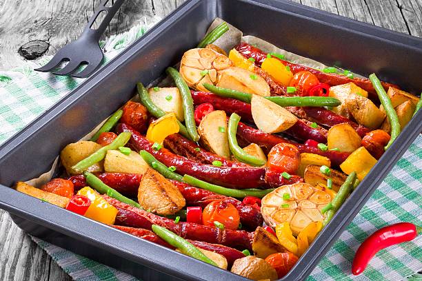 A tray of roasted sausages with mixed vegetables, including potatoes, green beans, and bell peppers.