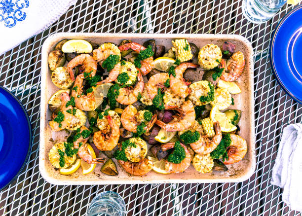 A platter of grilled shrimp with vegetables, garnished with green sauce and lemon wedges on a table