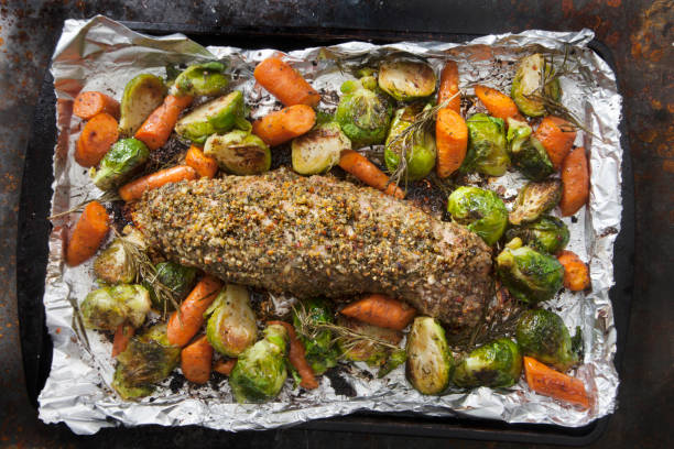 A roasted meatloaf surrounded by carrots and Brussels sprouts on a baking sheet covered with foil.