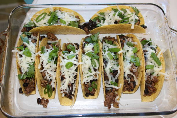 A platter of tacos filled with ground beef, black beans, shredded cheese, and green onions, arranged in a glass dish.