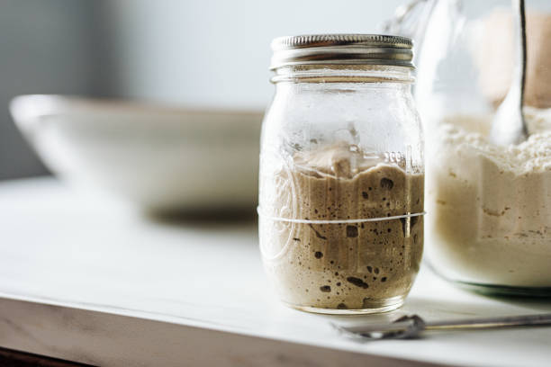 A jar of sourdough starter beside a bowl of flour on a kitchen countertop.