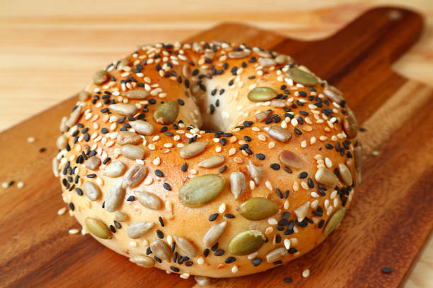 A seeded bagel topped with various seeds on a wooden cutting board.