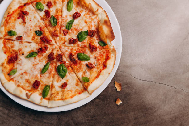 A freshly baked pizza topped with mozzarella cheese, sun-dried tomatoes, and fresh basil leaves on a white plate.