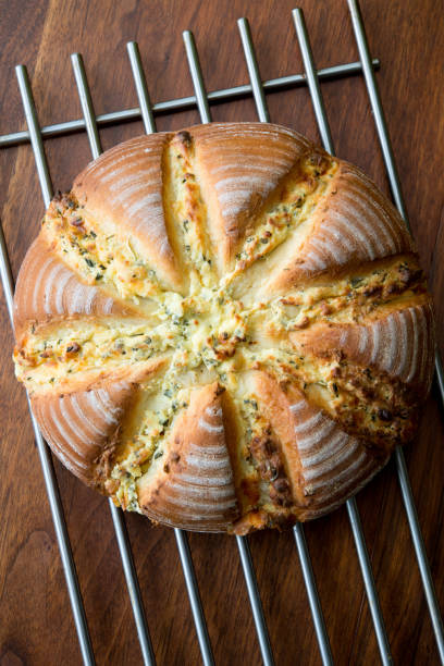 A round loaf of freshly baked bread with a golden crust and sliced design on top, resting on a cooling rack.