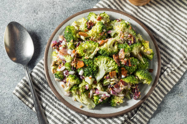 A healthy broccoli salad topped with bacon bits and chopped onions on a gray plate, sitting on a striped napkin.