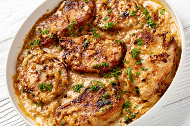 A dish of creamy pork chops garnished with parsley on a light wooden surface