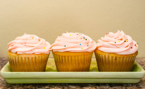 Three delicious cupcakes with pink frosting and colorful sprinkles on a green tray