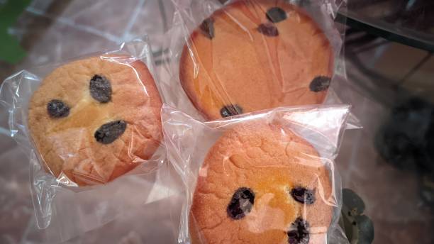 Three cookies with chocolate chips, packaged and smiling faces, placed on a table.