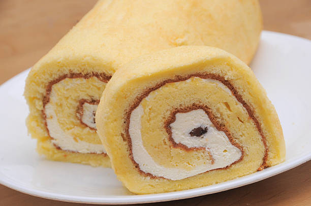 Close-up of a sliced yellow cake roll with cream filling on a white plate.