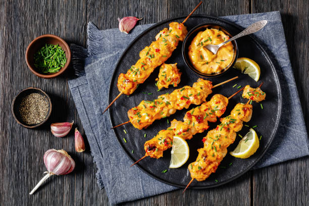 Grilled skewers with a creamy sauce and lemon on a black plate.