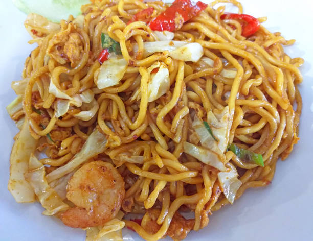 A close-up of stir-fried noodles with shrimp, vegetables, and spices.