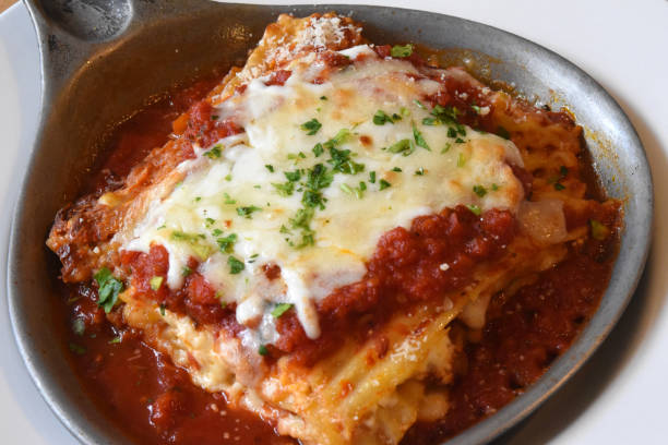 A serving of lasagna topped with melted cheese and garnished with parsley in a metal dish