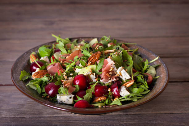 A vibrant salad with mixed greens, grapes, nuts, and cheese served in a rustic bowl on a wooden table.