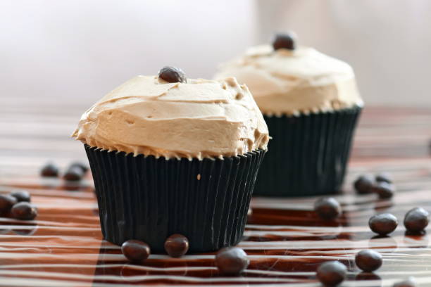 Two chocolate cupcakes with creamy frosting and coffee beans on top, displayed on a wooden surface.