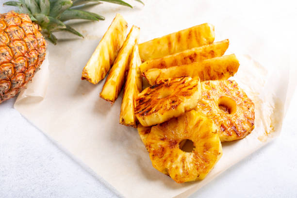 Grilled pineapple slices and spears on a light background with a whole pineapple on the side