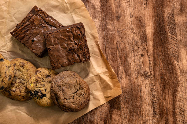 A selection of cookies and brownies on crumpled parchment paper on a wooden surface