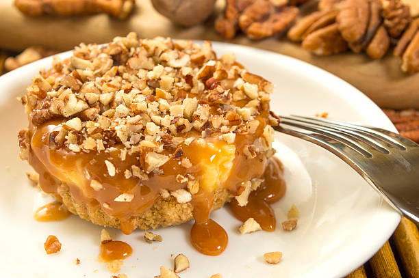 A delicious dessert featuring a layer of creamy filling drizzled with caramel and topped with chopped pecans on a white plate.