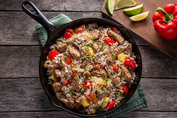 A cast iron skillet filled with a colorful mixture of rice, beef, red and yellow bell peppers, and pineapple, garnished with green onions, placed on a rustic wooden surface.