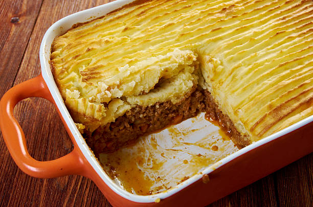 A baked shepherd's pie in an orange casserole dish, with a portion cut out, revealing the meat filling underneath creamy mashed potatoes.