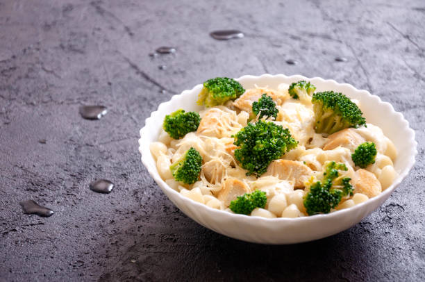 A bowl of pasta with broccoli and a creamy sauce on a dark textured surface.